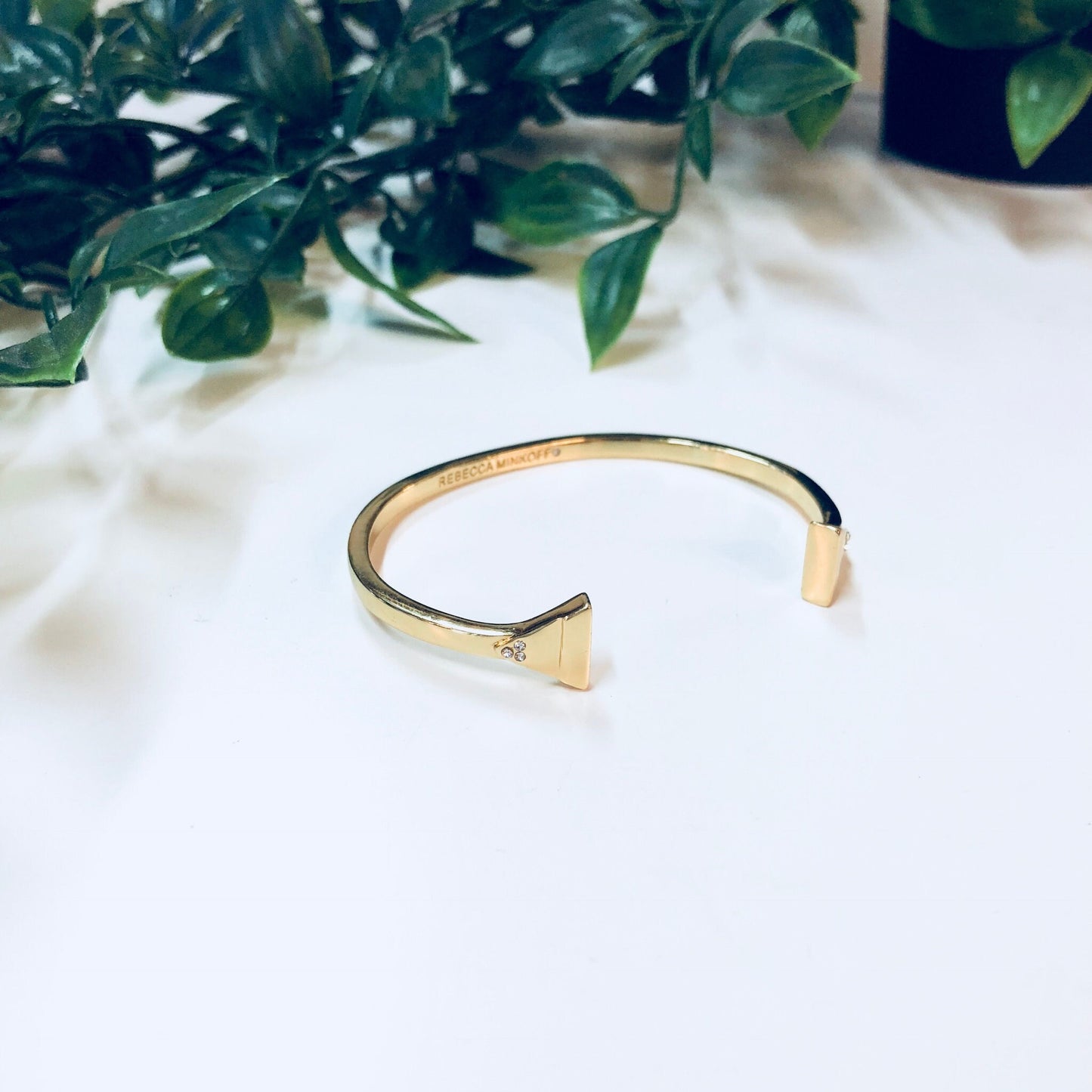 Gold toned cuff bracelet with triangle accents resting on white fur, with green foliage in the background.