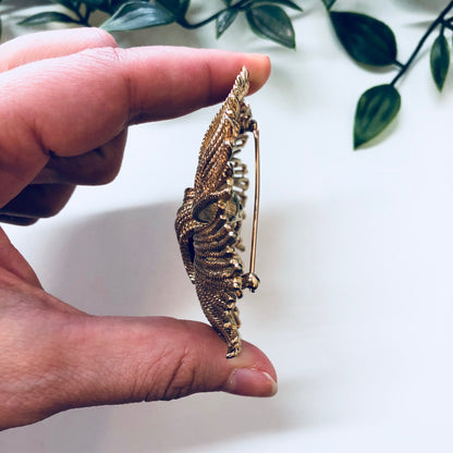 Vintage gold-toned swirl brooch by Monet, held in hand against white background with green foliage.