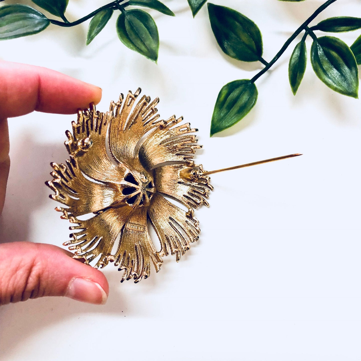 Vintage gold-toned swirl brooch by Monet, held in front of green leaves, showcasing unique statement jewelry from the brand.