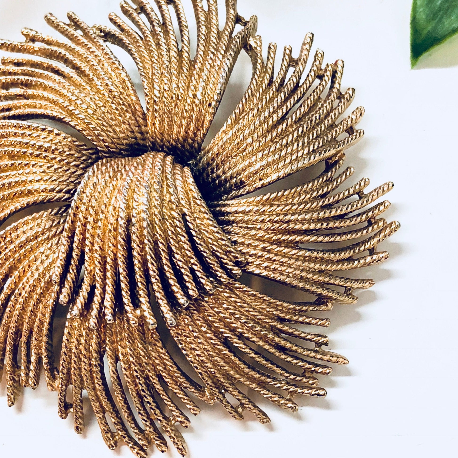 Vintage gold-toned swirl brooch by Monet, featuring intricate layered wire design. Unique statement jewelry piece from a renowned vintage brand.