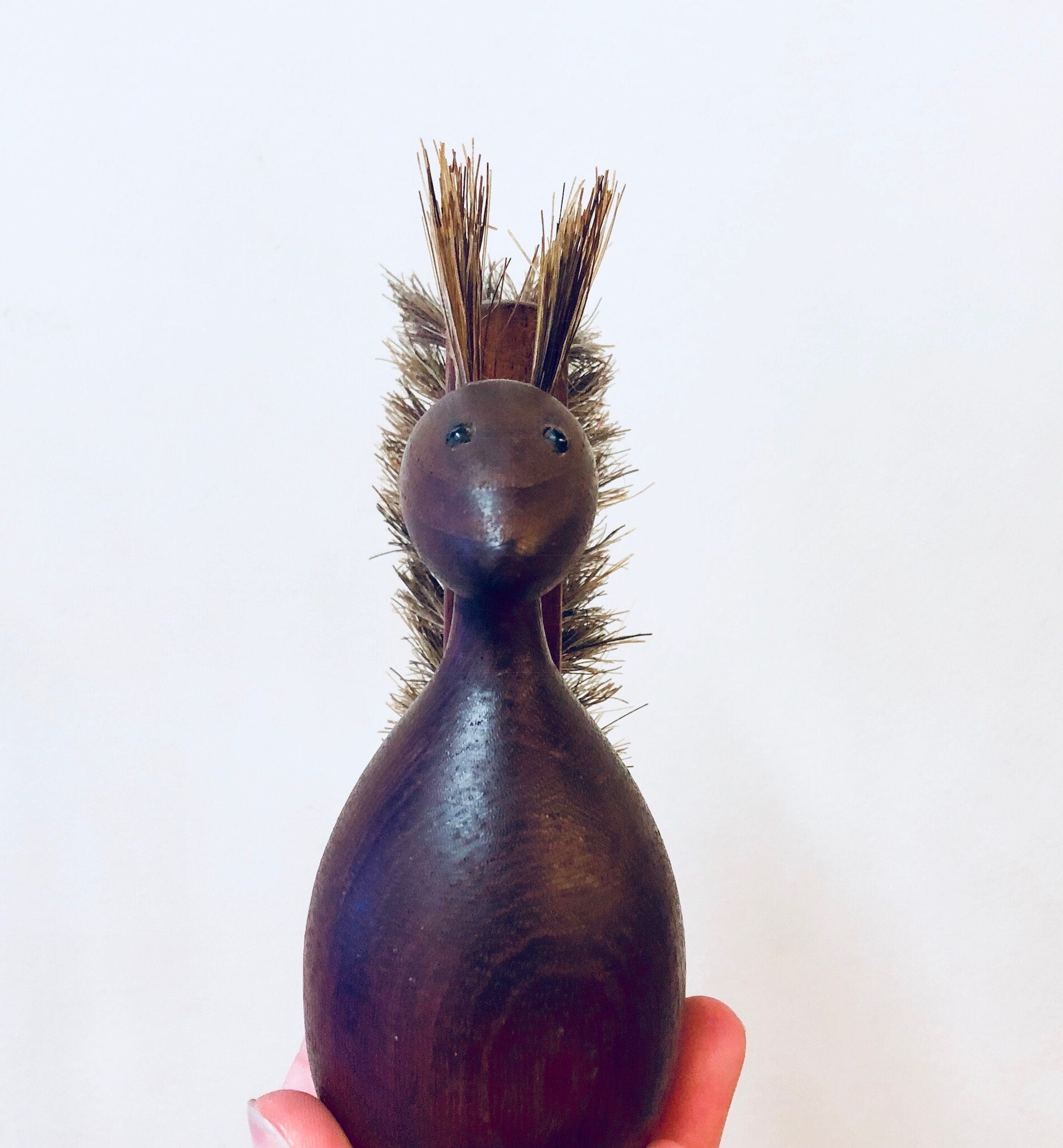 Vintage wooden squirrel-shaped scrub brush with bristle hair and carved details, held in hand against white background, rustic home decor accent in shades of brown and purple.