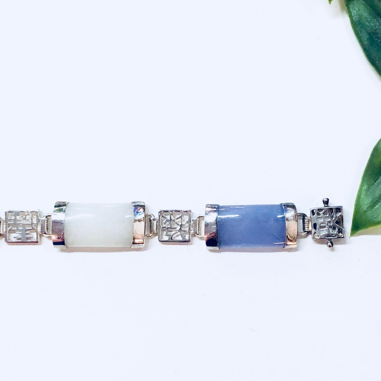 Vintage silver link bracelet with colorful natural stones including jade, purple, orange, white and red cabochons, displayed on a white background with green leaves.