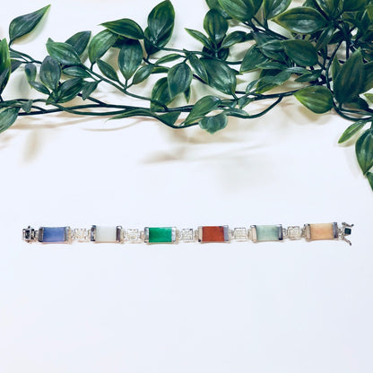 Vintage sterling silver link bracelet with natural stones in jade, purple, orange, white and red, adorned with Asian-inspired design elements, set against a lush green leaf background.