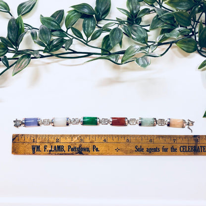 Vintage sterling silver link bracelet with assorted natural stone charms in jade green, purple, orange, white and red hues, displayed with a ruler and leafy green plant branches above on a white background.