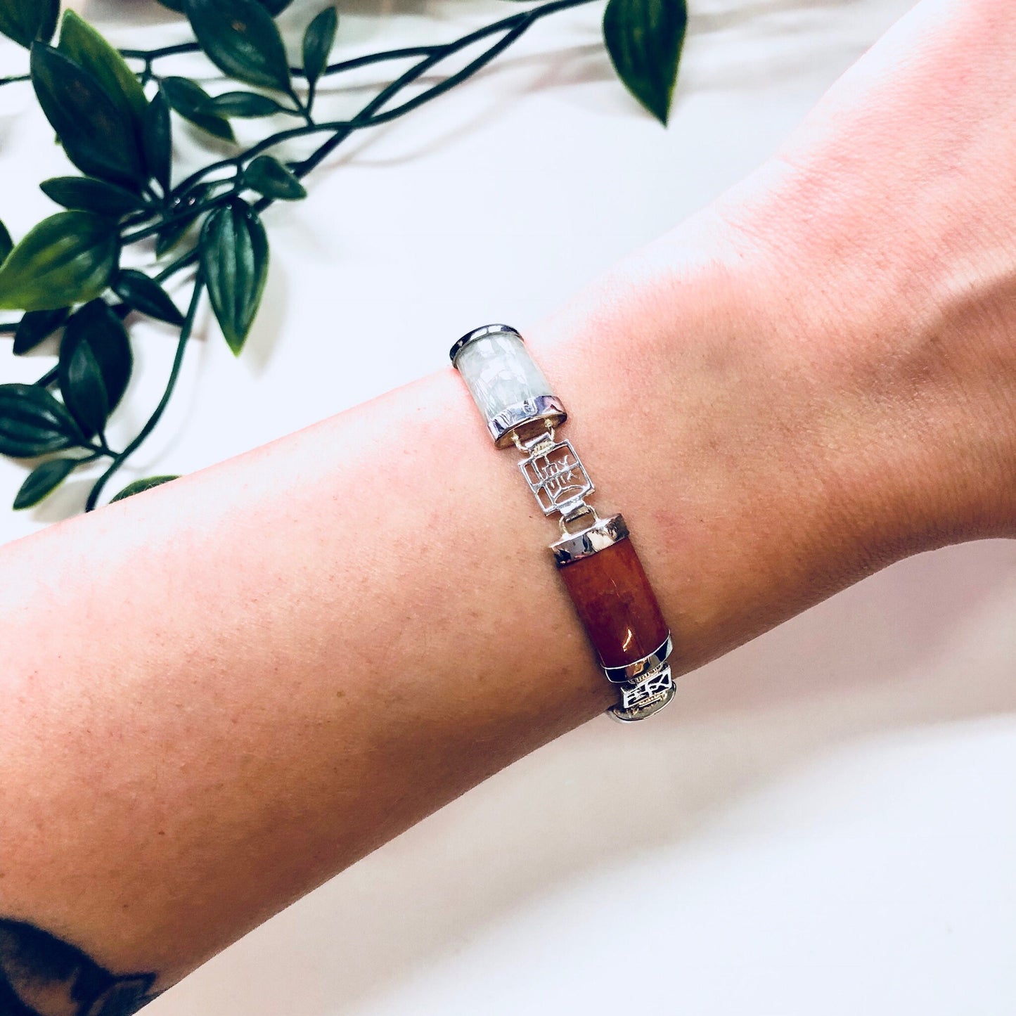 Vintage sterling silver link bracelet with natural jade stones in purple, orange, white, and red hues on a wrist with greenery in the background.