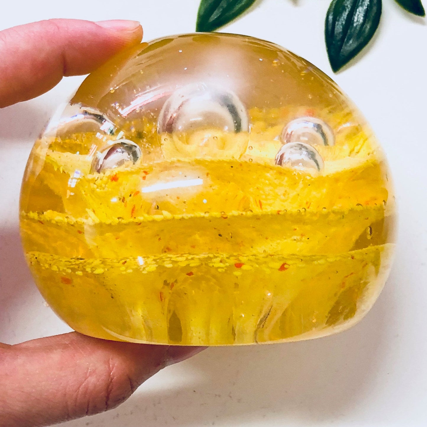 Yellow and orange speckled glass paperweight with colorful design held in hand against a white background with green leaves, vintage office decor.