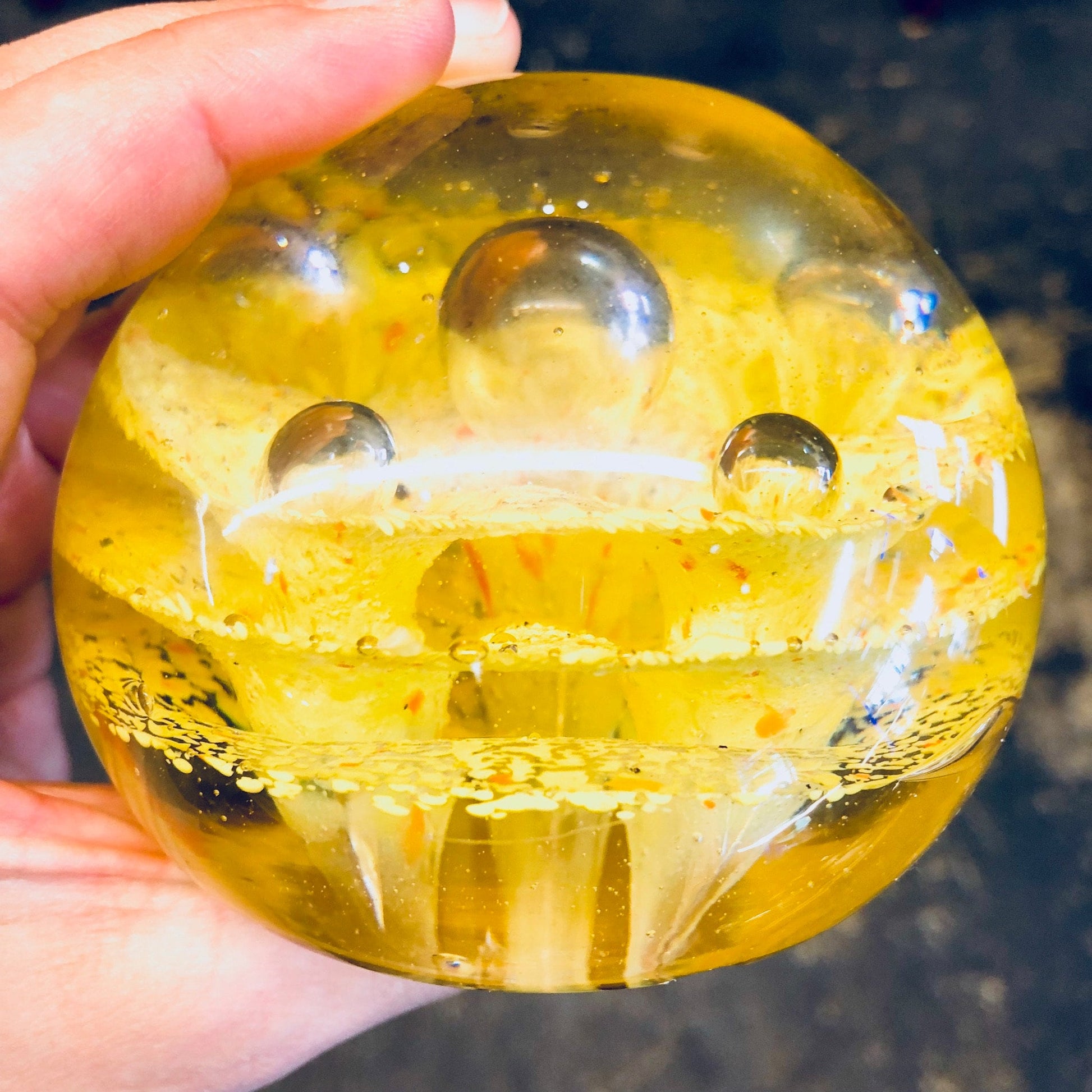 Alt: Hand holding a yellow and orange speckled glass paperweight with colorful design, ideal for vintage office decor.