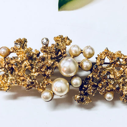 Vintage gold-toned brooch with faux pearls and textured gold-colored metal forming an ornate statement piece of costume jewelry.