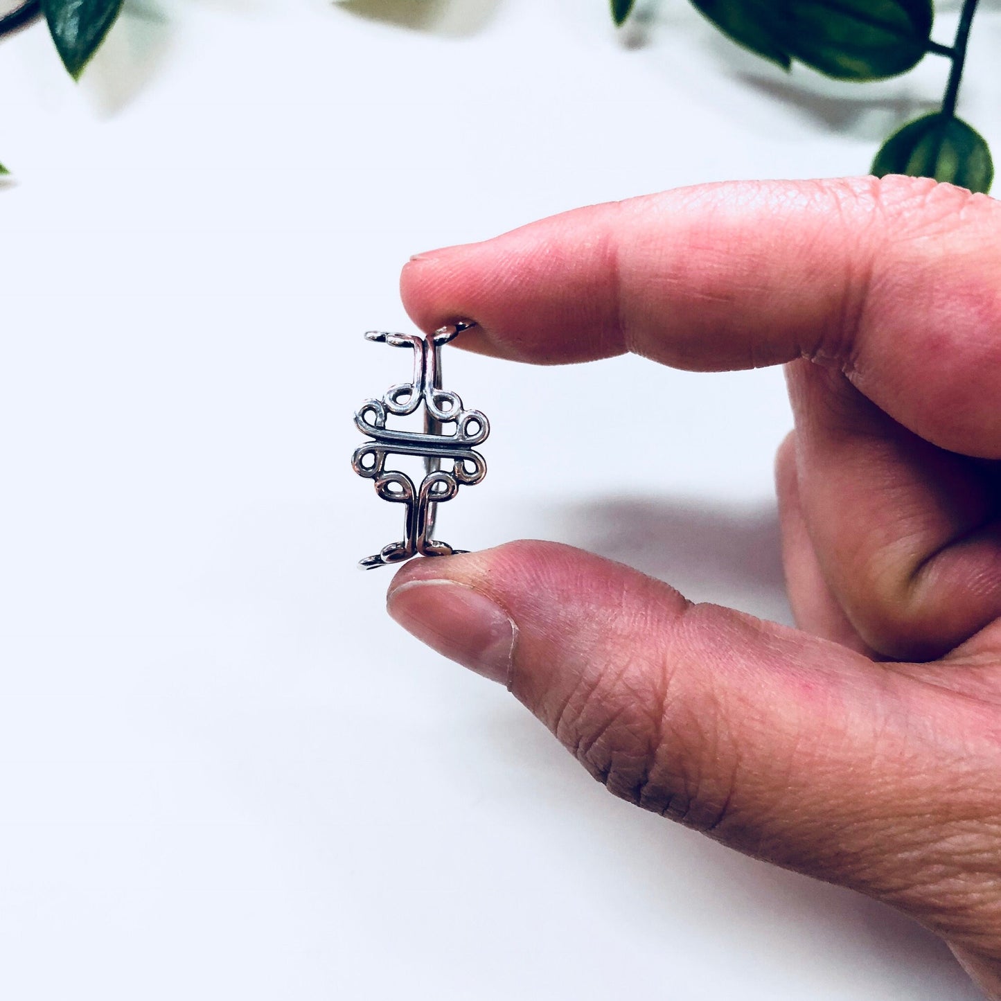 Man's hand holding a small vintage sterling silver ring with a cut-out design against a white background with green foliage.