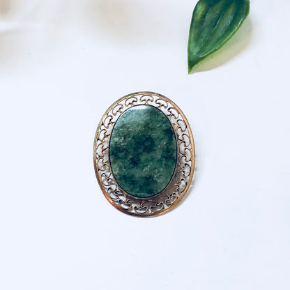 Vintage 12K gold filled brooch with green and white stone, decorative gold scrollwork border around the oval-shaped green gemstone, shown on white background with green leaf accent.