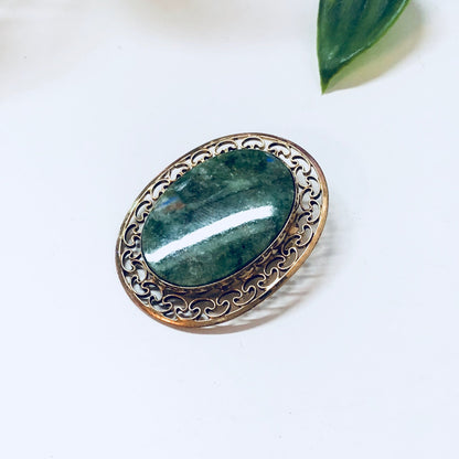 Vintage gold filled brooch with green stone and intricate filigree design, set against a white background with green leaf accent.