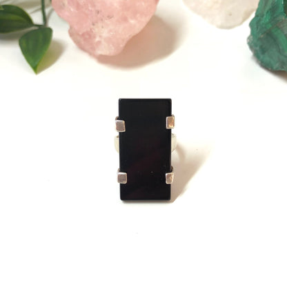 Vintage sterling silver rectangle ring with black onyx stone on white surface with rose quartz and green leaves in background, minimalist jewelry