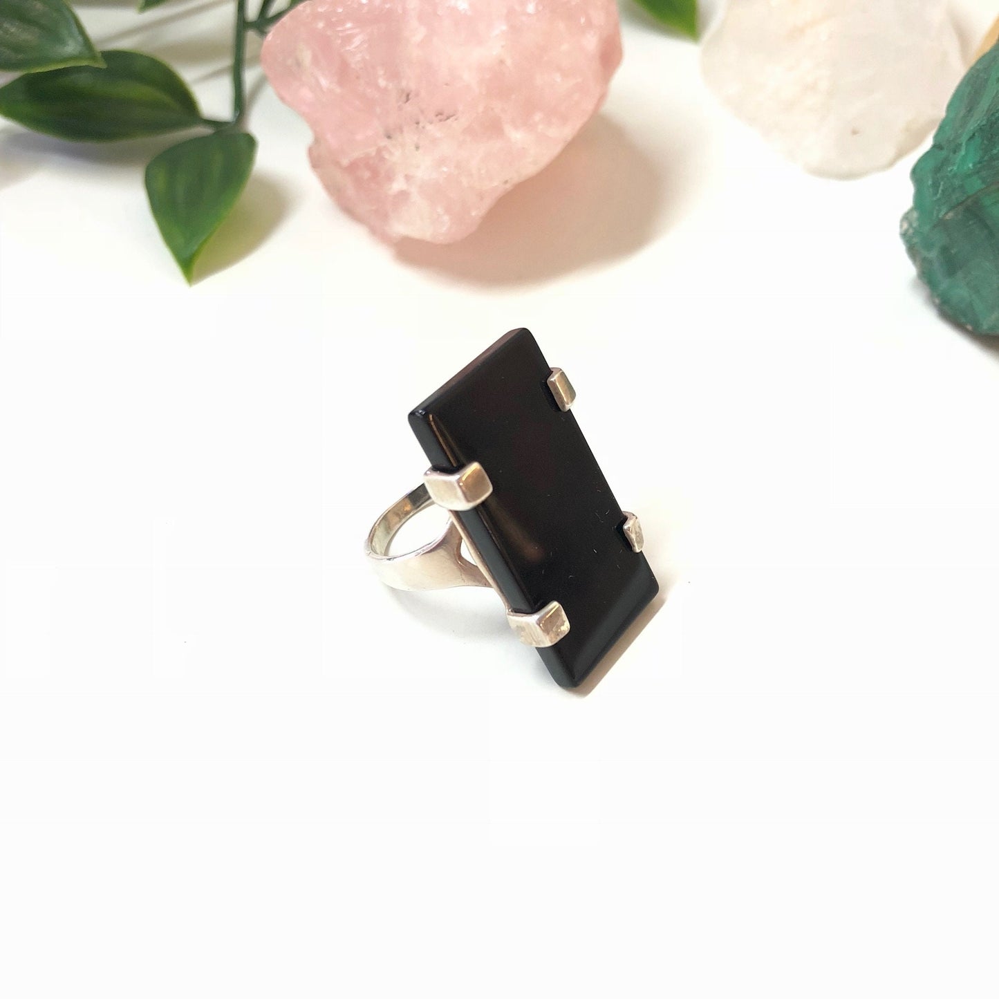 Vintage sterling silver ring with rectangular black onyx stone on white background with pink quartz and greenery