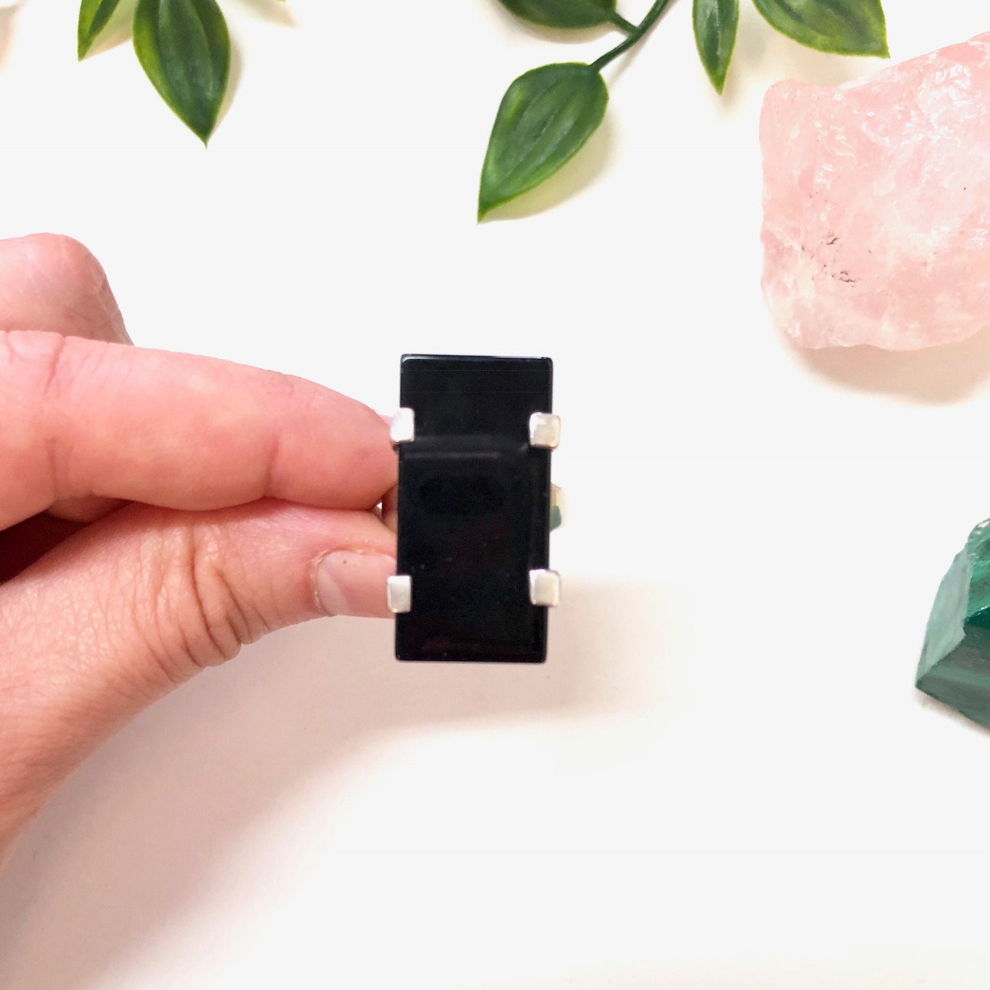 Vintage black onyx sterling silver minimalist ring held in front of green leaves and pink quartz stones