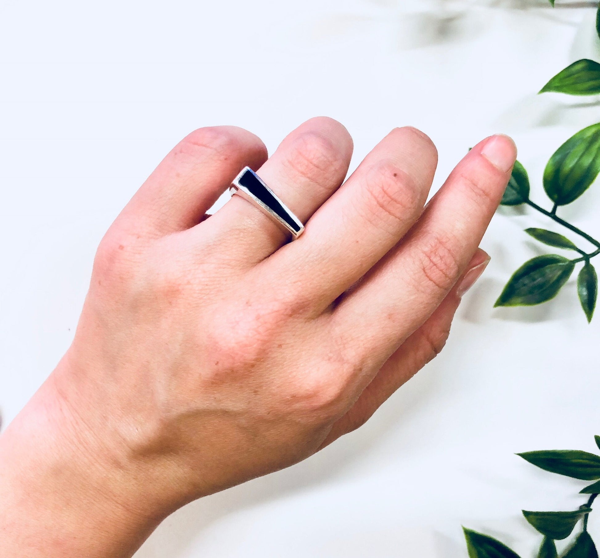 Vintage sterling silver ring with black onyx inlay on a person's hand, next to green leaves. Simple, abstract jewelry perfect for an anniversary gift.