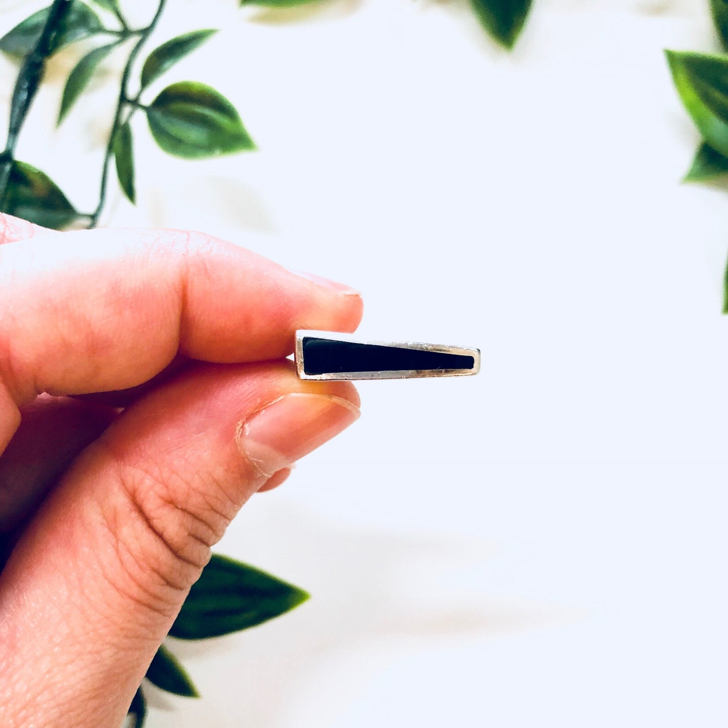 Hand holding a vintage sterling silver ring with a rectangular black onyx stone against a leafy background.