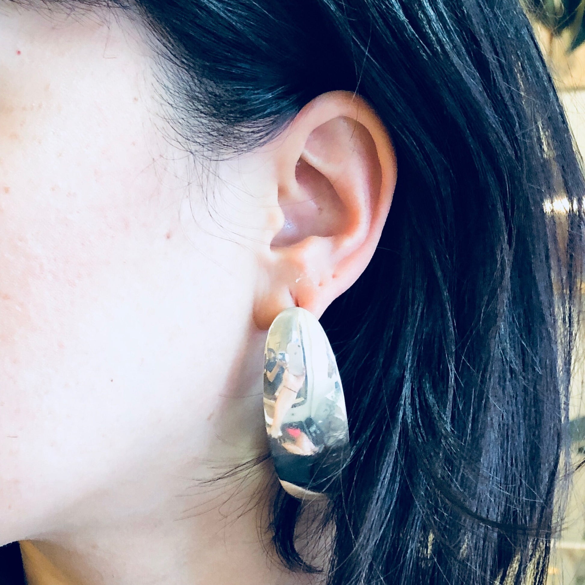 Close-up of a woman's ear wearing a large, vintage silver earring with an abstract, minimalist design against her dark hair.