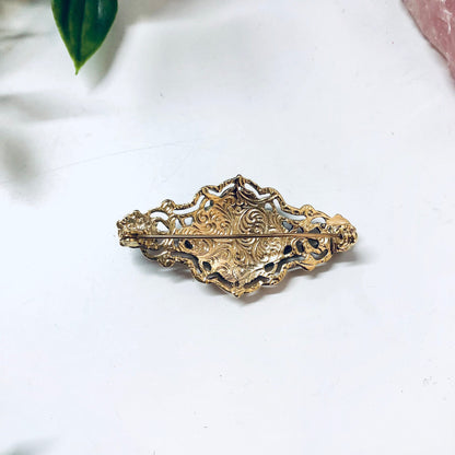 Vintage gold-toned floral brooch pin, ornate costume jewelry piece on white background with rose in soft focus behind