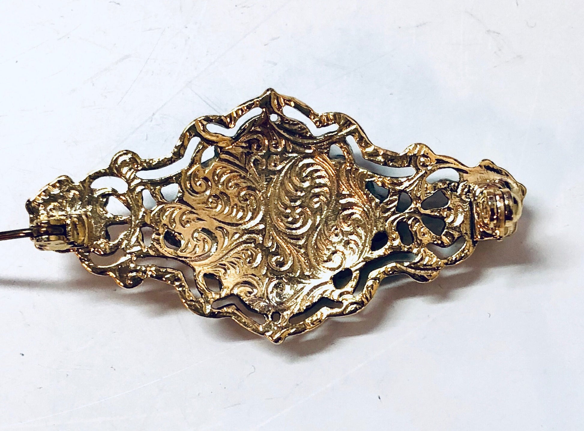 Vintage gold-toned floral brooch pin with intricate filigree design and black enamel accents, antique costume jewelry piece.