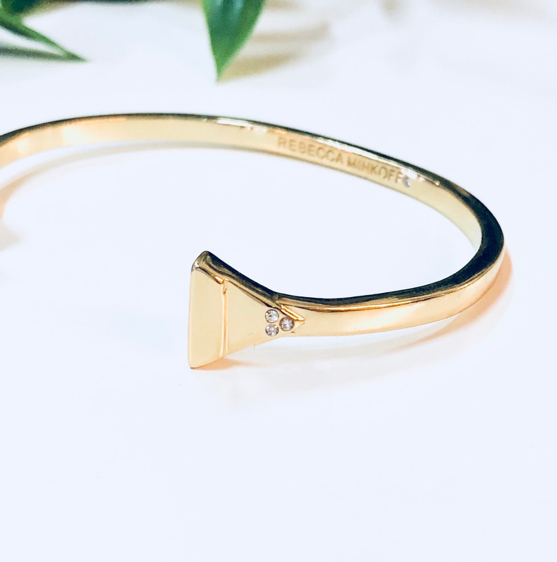 Gold toned cuff bracelet with triangle shape detail, minimal design, on white background with leaves.