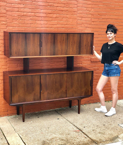 Mid-century modern teak credenza in front of a brick wall, with a smiling woman in shorts and a black shirt standing next to it on a concrete sidewalk.