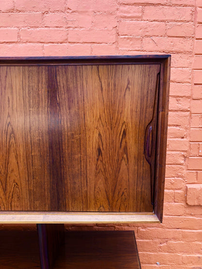 Beautiful mid-century modern teak credenza against a pink brick wall, showcasing the rich wood grain and minimalist design characteristic of MCM furniture.