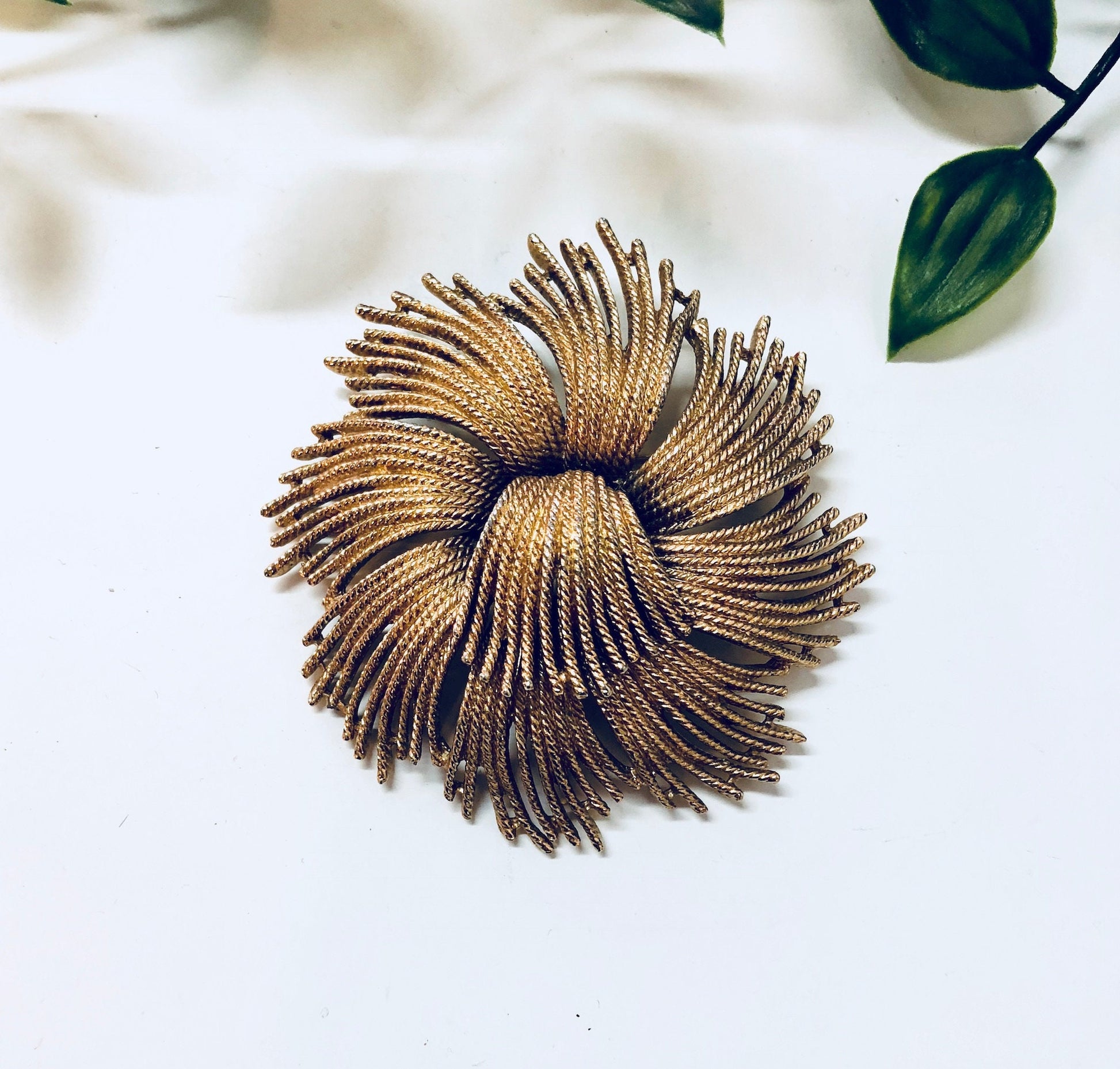 Vintage gold-toned Monet brooch featuring a unique swirl design, making a bold statement as a piece of jewelry. The large pin is an eye-catching accessory from the brand's vintage collection.