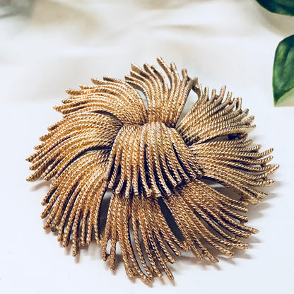 Vintage gold-toned swirl brooch by Monet, a large statement jewelry piece with unique radiating textured design, shown on white background.