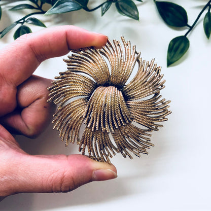 Vintage gold-toned swirl brooch by Monet, held in hand against white background with green leaves