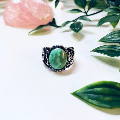 Vintage silver turquoise ring with textured band displayed on white surface with green leaves and pink crystal in background