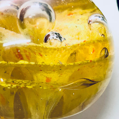 Close-up of a yellow glass paperweight with speckled orange design and air bubbles, vintage office decor.