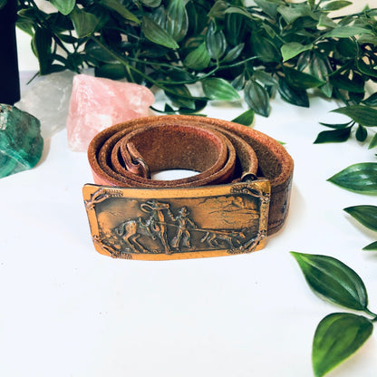 Vintage brown leather cowboy belt with embossed western design and hook buckle, surrounded by green leafy plants and pink crystal