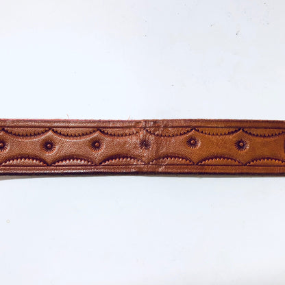 Vintage brown leather cowboy belt with intricate tooled designs and a hook buckle closure, featuring a southwestern style pattern on a skinny belt strap.