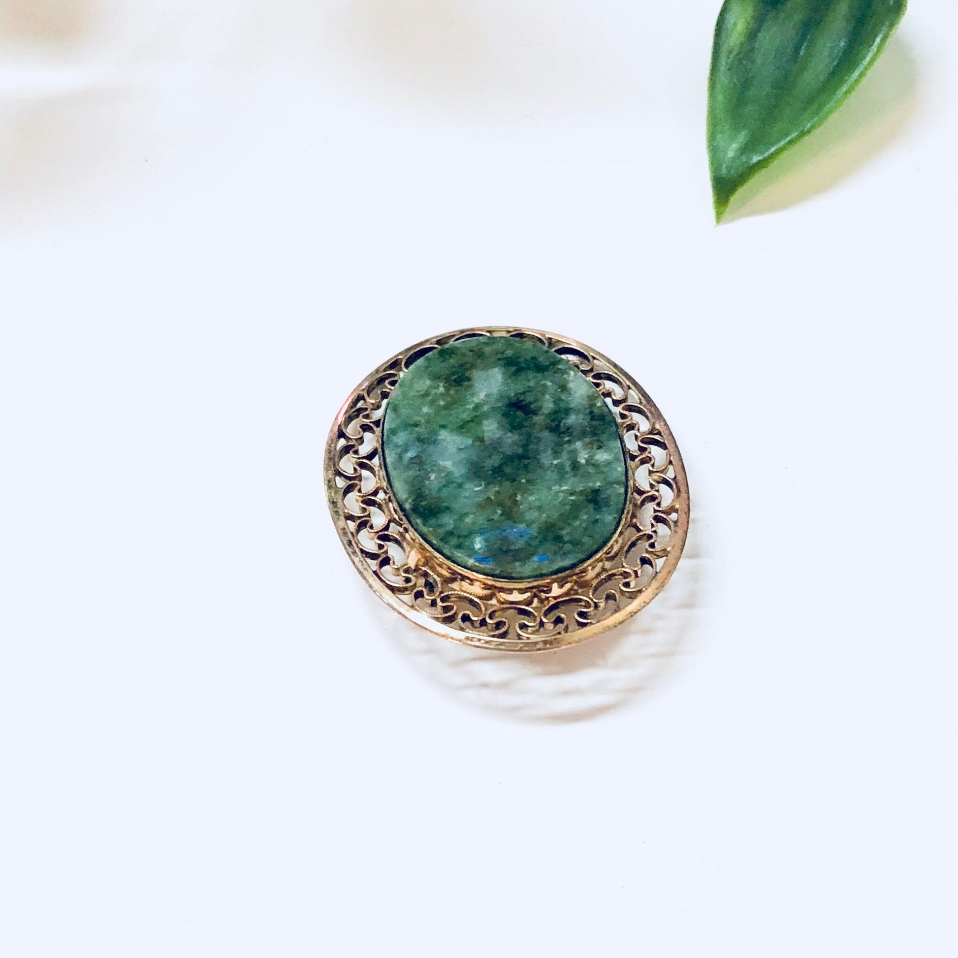 Vintage 12K gold filled brooch with green stone and intricate gold detailing, set against a white background with green leaf accents.