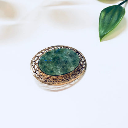 Vintage 12K gold filled brooch with green stone, decorative filigree border, displayed on white background with green leaf accents.