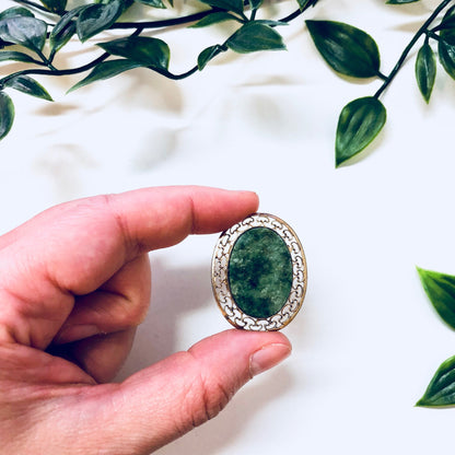 Vintage 12K gold filled brooch with green and white stone, held in hand with greenery in background