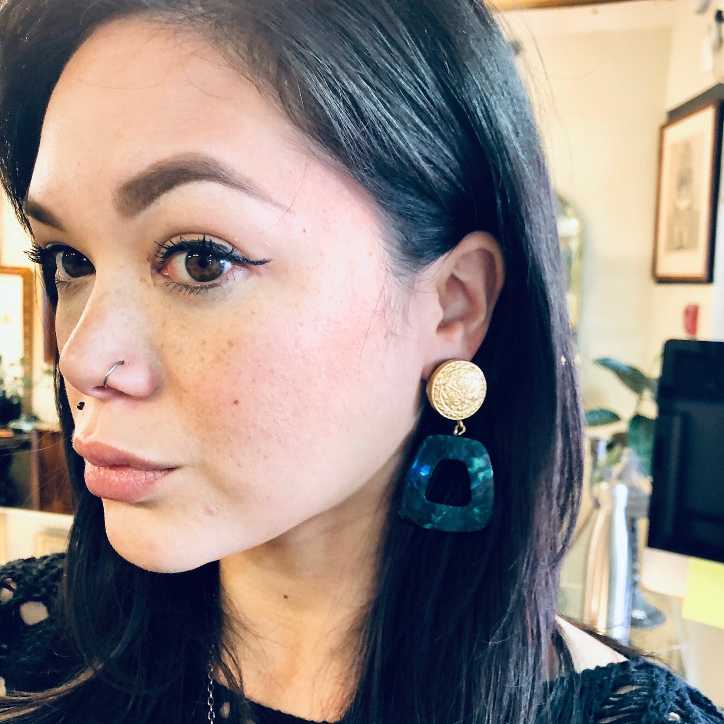 Close-up portrait of a woman with long black hair wearing green and gold dangle earrings with a marble design.