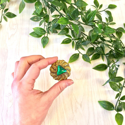 Vintage gold tone brooch pin with green feather design on wooden surface surrounded by green leaves, perfect for Valentine's Day or costume jewelry accessory.