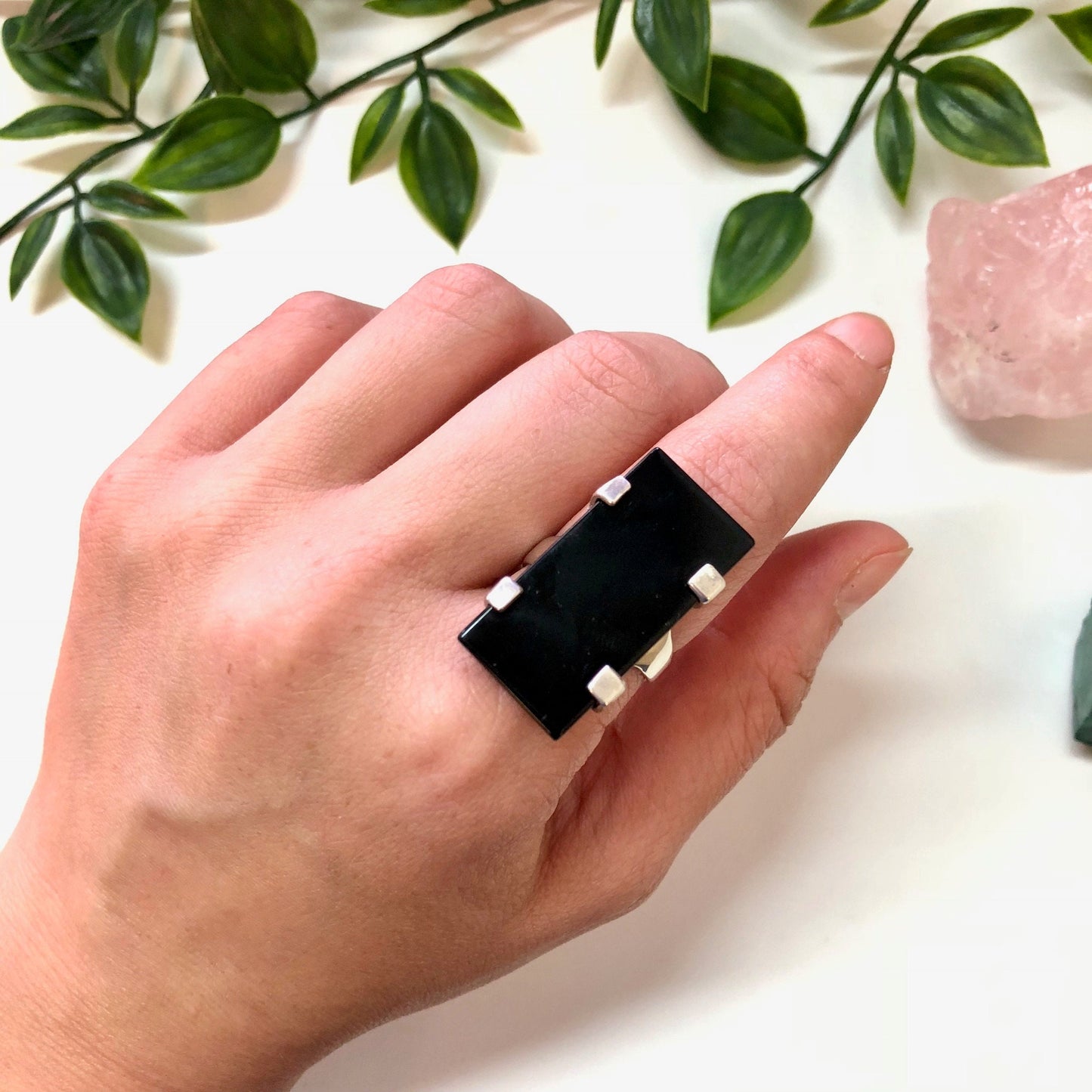 Vintage sterling silver ring with black onyx stone on hand next to rose quartz crystal and green leaves