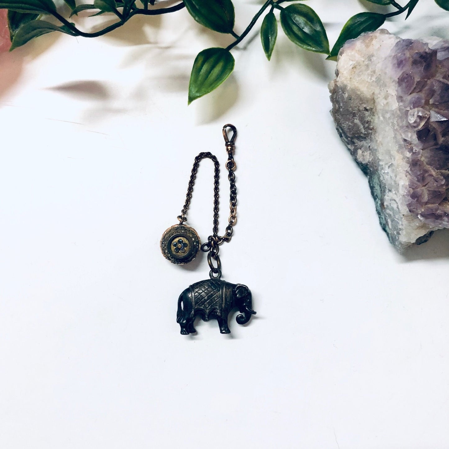 Vintage sterling silver elephant watch fob and engraved ball chain displayed with amethyst crystal and foliage.