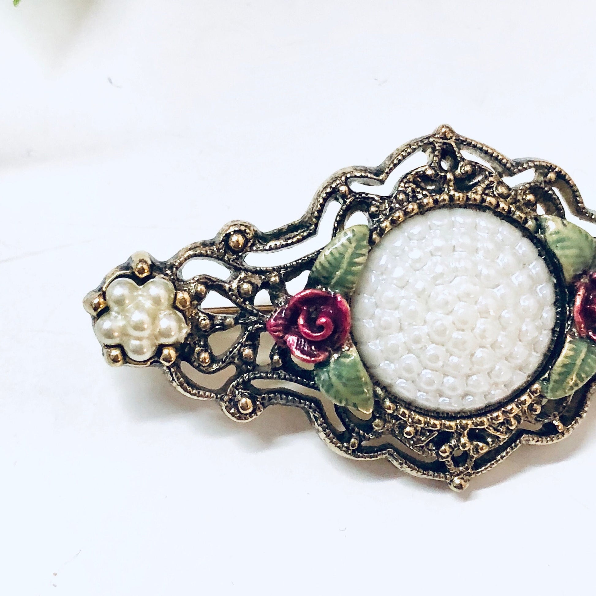 Vintage gold-toned brooch with floral design, featuring white textured center stone surrounded by green leaves and pink flower accents, ornate metal filigree detailing