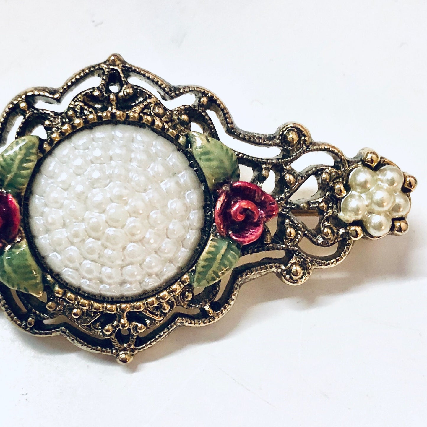 Vintage gold-toned floral brooch with intricate filigree design, faux pearls, and colorful enamel accents, a beautiful piece of costume jewelry from the past.