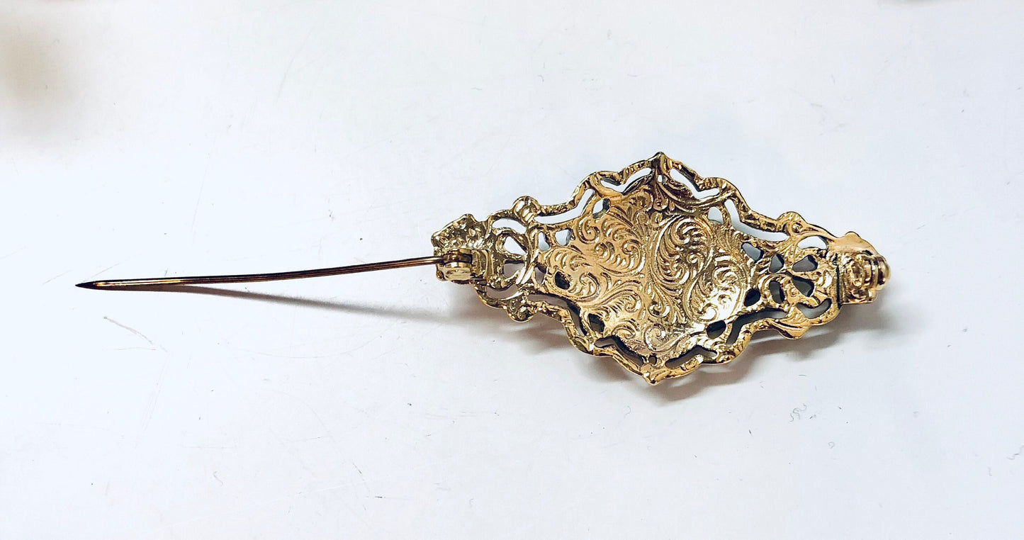 Vintage gold toned floral brooch pin, ornate decorative costume jewelry piece with detailed metalwork design.