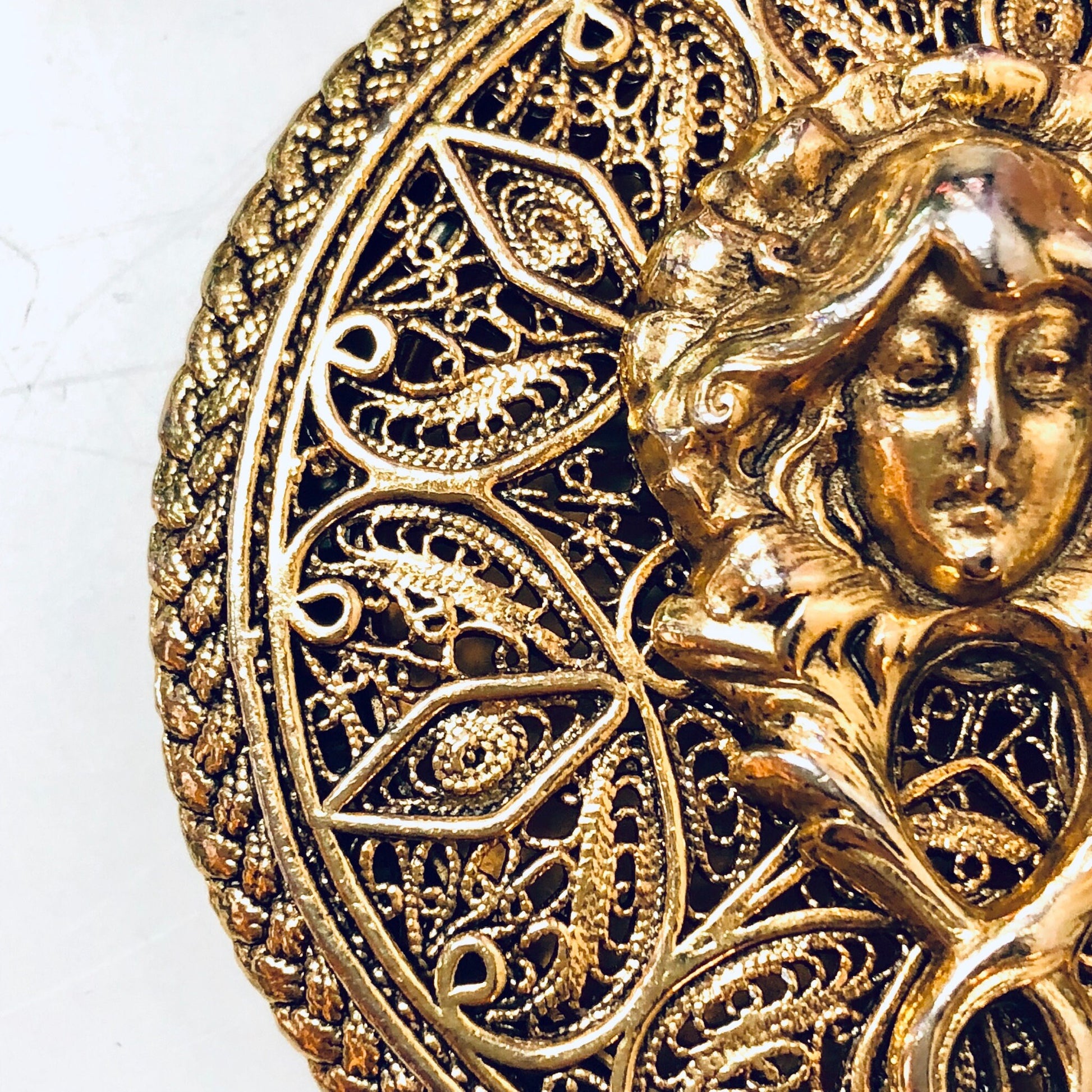 Ornate vintage gold-toned locket pendant featuring an intricate filigree design and a sculpted lady's face