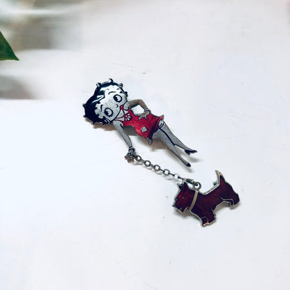 Betty Boop enamel pin featuring the cartoon character in a red dress holding a black and white dog, with a silver-tone chain attached, against a white background.