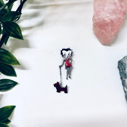 Betty Boop vintage silver tone pin with her dog, featuring red and black enamel accents, set against a white background with pink quartz and green leaves.