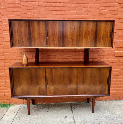 Mid century modern hardwood teak credenza with two cabinets and open shelf, against a brick wall background