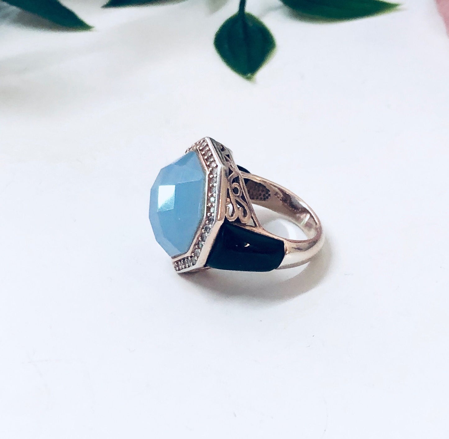 Vintage sterling silver cocktail ring with light blue and dark purple stones in an ornate filigree setting, shown against a white background with leaves.