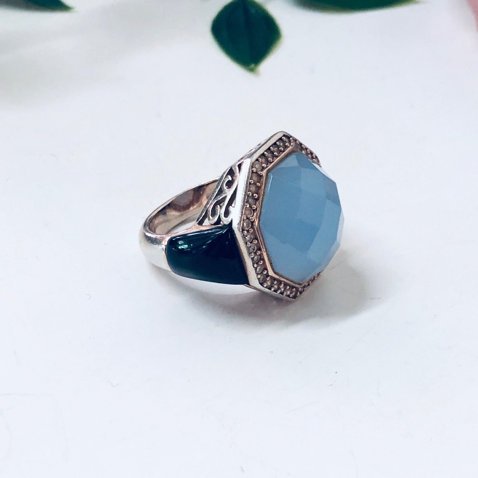 Vintage sterling silver cocktail ring with light blue stone and intricate filigree detailing on the band, set against a white background with leaves.