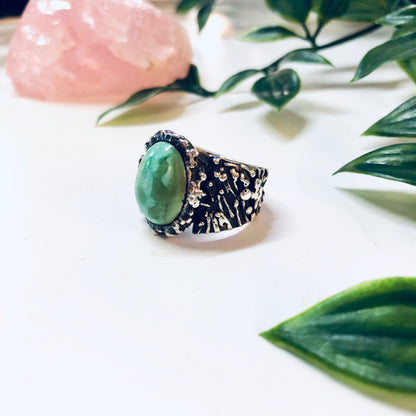 Vintage sterling silver ring with large oval turquoise stone surrounded by textured silver band, set against green leaves and rose quartz crystal.